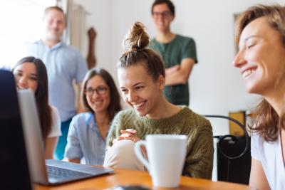 Grupp med människor tittar på en laptop och ler